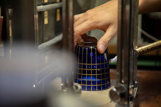 Hand placing a blue ceramic cup with gold grid pattern on a manufacturing machine