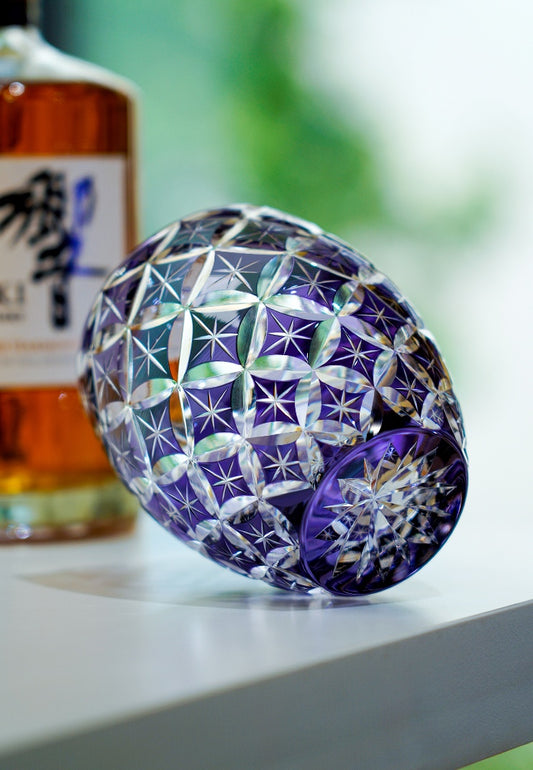 Rin Essense purple cut crystal whiskey glass lying on its side with amber bottle blurred in background
