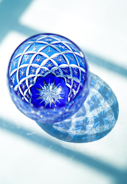Rin Essense blue cut crystal whiskey glass with star pattern casting decorative shadow on white surface