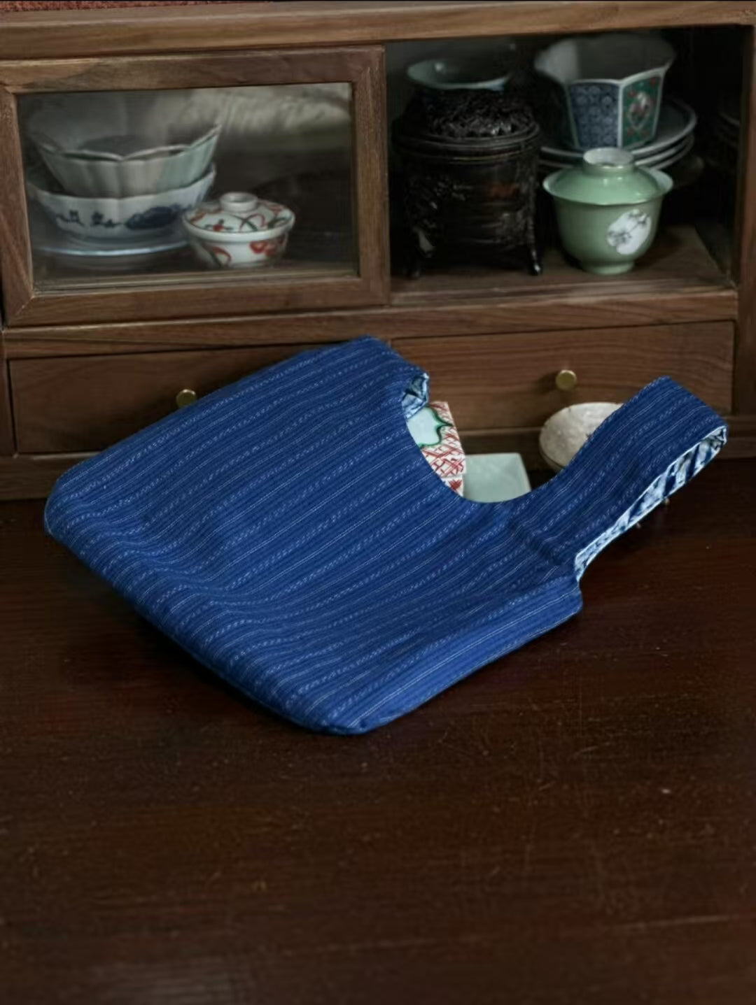 Indigo Shibori knot bag by Rin Essense flat on dark wood table showing blue striped exterior and patterned lining