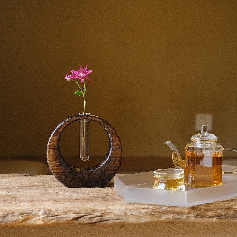 Rin Essense japanese vase with circular wooden frame and single pink flower on rustic wooden table