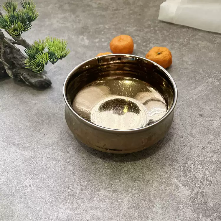 Rin Essense polished metal bowl on gray surface with small green plant and two oranges nearby