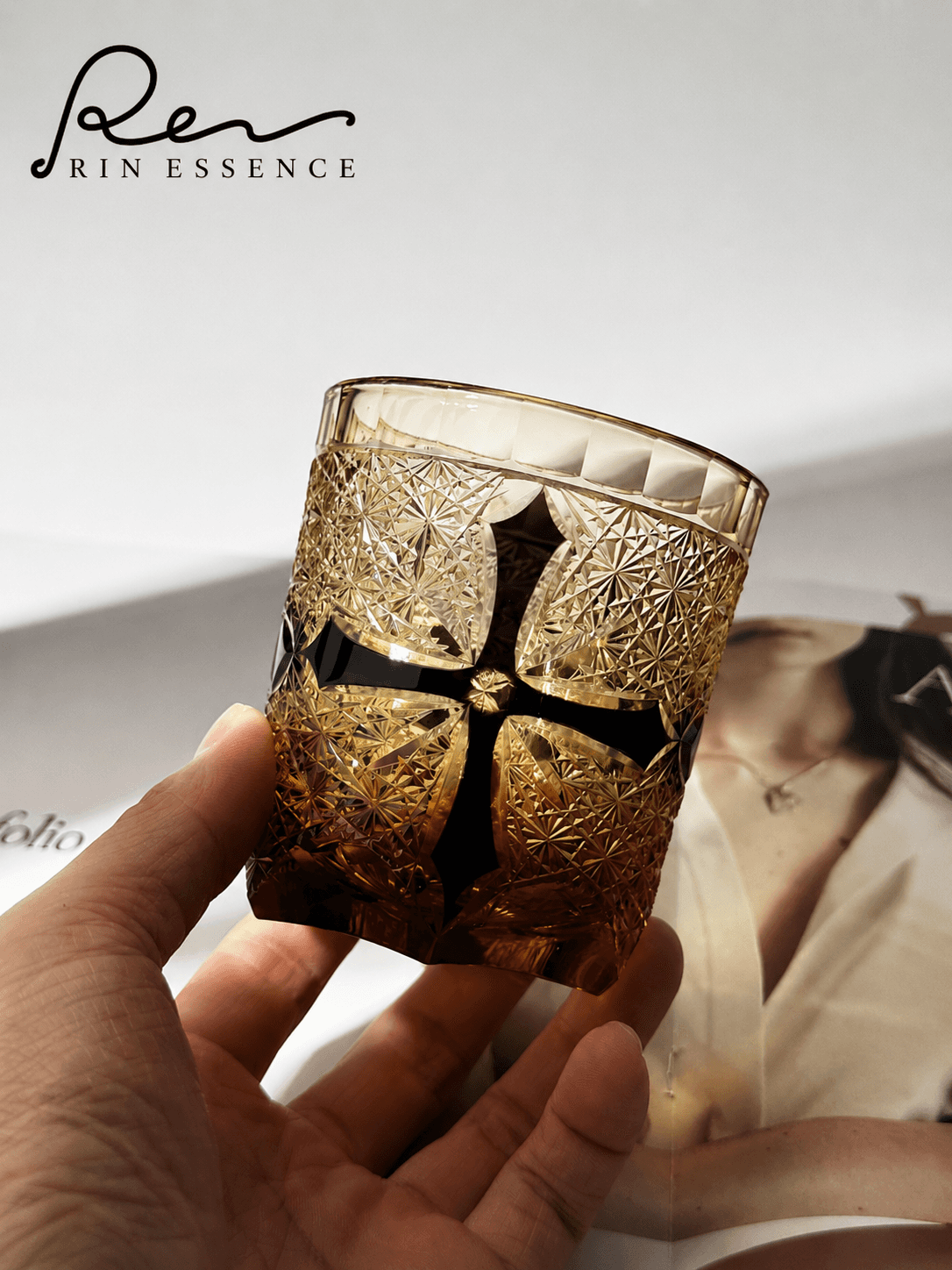 RIN ESSENCE whiskey glass with amber tint and black cross design held in hand