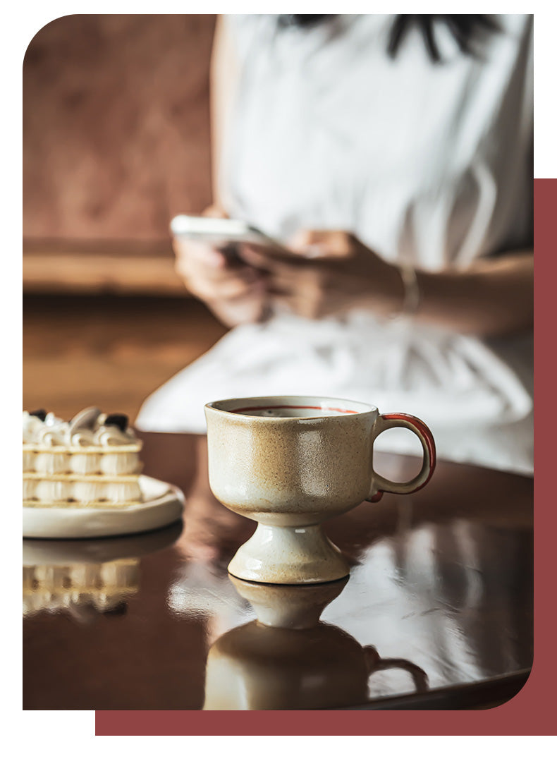 Japanese vintage ceramic cup on pedestal mug beside dessert on cafe table with blurred woman in background