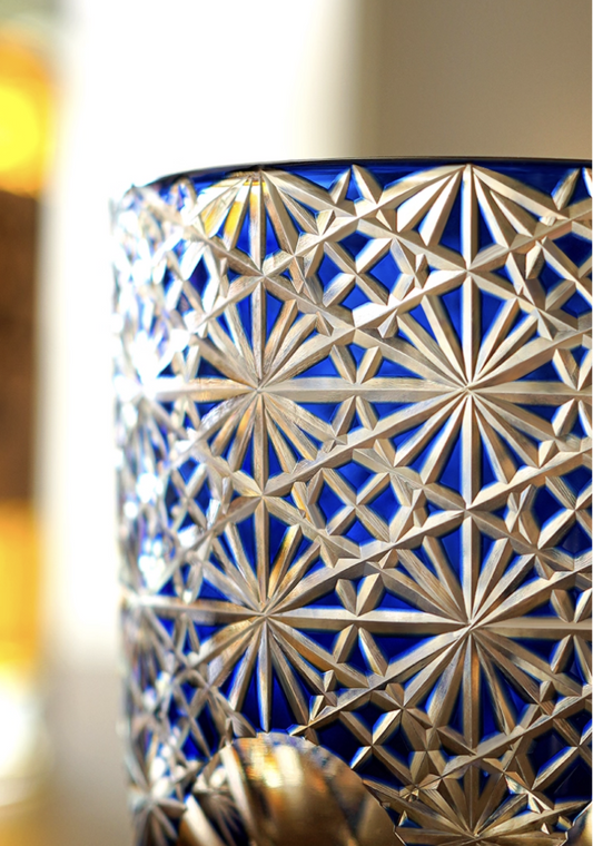 Close up of Rin Essense Edo Kiriko whisky glass in cobalt blue with intricate starburst cut pattern and amber background