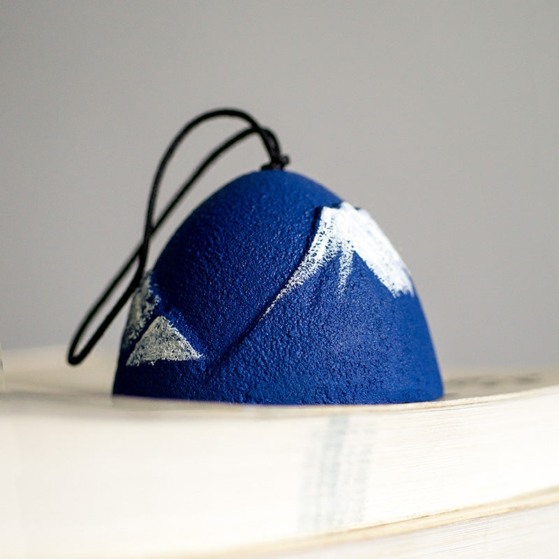 Rin Essense blue textured dome pendant with white mountain design and black cord resting on a book