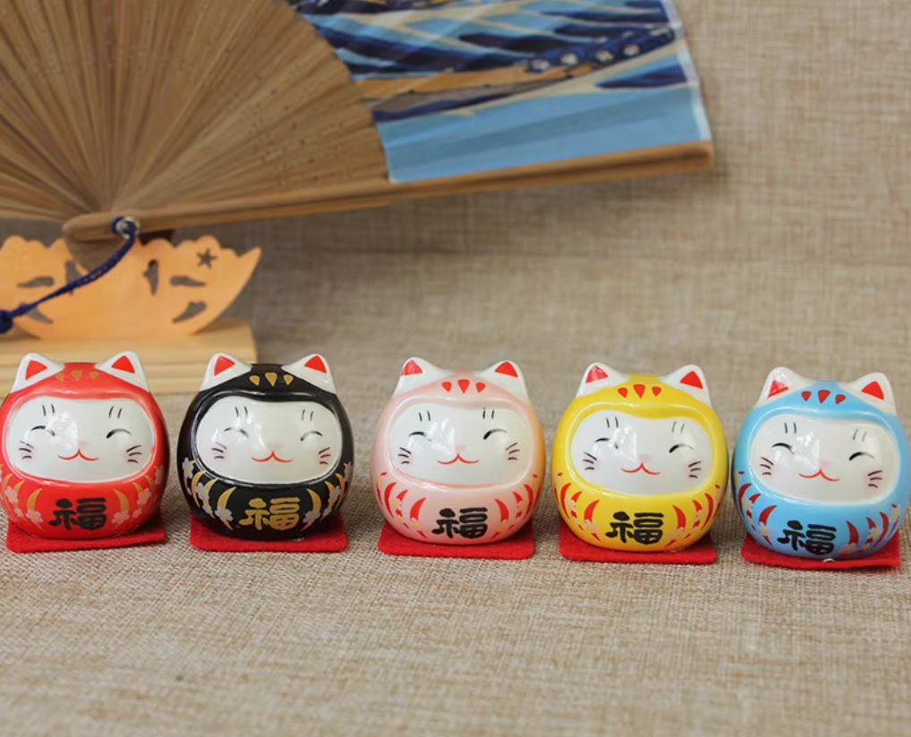 Five colorful ceramic cat daruma tumbling doll ornament figurines in red black white yellow and blue