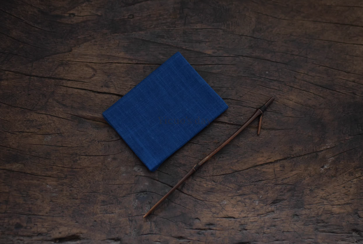 Japanese Indigo Tea Cloth – Hand-Dyed Cotton Linen folded on rustic wooden surface with a thin wooden stick