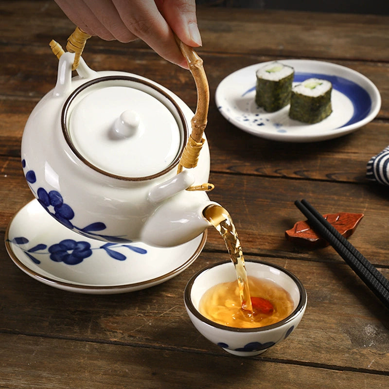 Kokoro ceramic tea set white teapot with blue floral design pouring tea into small cup on wooden table