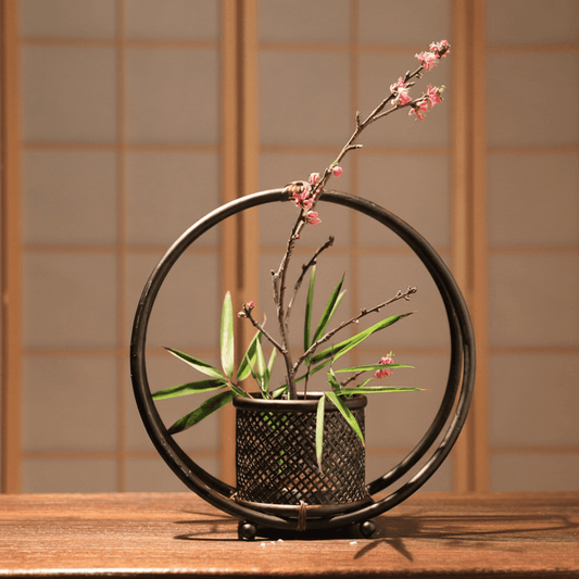 Rin Essense home décor featuring a black circular frame vase with green leaves and pink blossoms