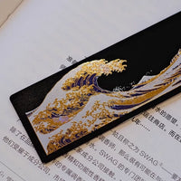 Black lacquer bookmark with gold and blue wave motif and red tassel on open book handcrafted lacquerware bookmarks