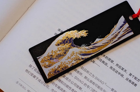 Black lacquer bookmark with gold and blue wave motif and red tassel on open book handcrafted lacquerware bookmarks