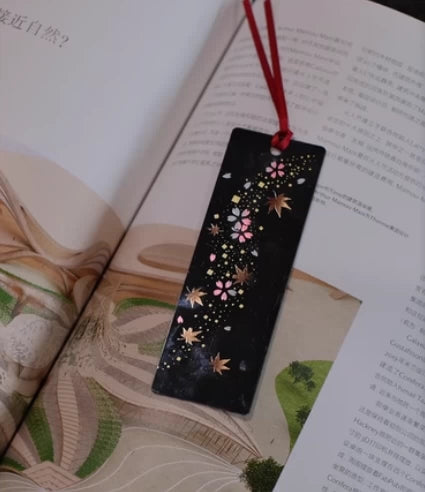 Rin Essense handcrafted lacquerware bookmarks black rectangular bookmark with pink flowers gold leaves and red cord on open book