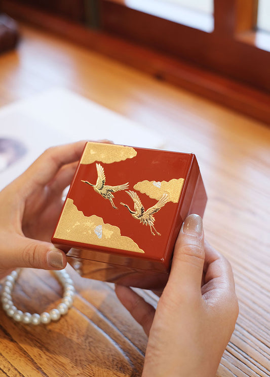 Rin Essense red Japanese lacquerware jewelry box with gold crane motifs held over wooden table