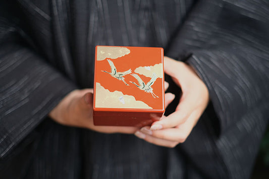 Woman in kimono holding Japanese lacquerware jewelry box with red lacquer cranes and gold cloud motifs
