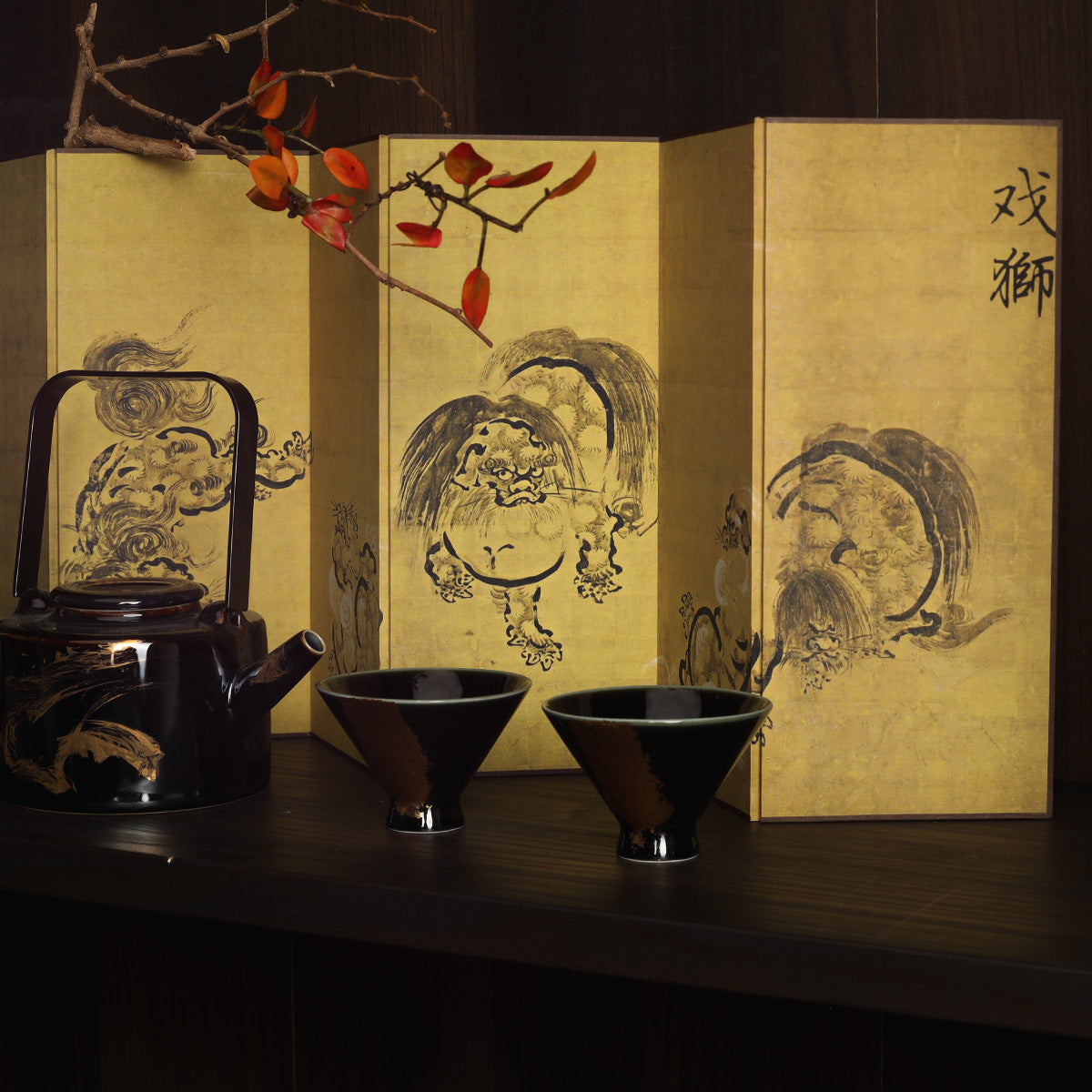 Rin Essense tea set with black teapot and cups in front of a gold Washi shoji folding screen with ink lion art