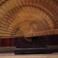 Golden nanmu wood folding fan displayed on an ornate black stand showcasing fine wood grain details