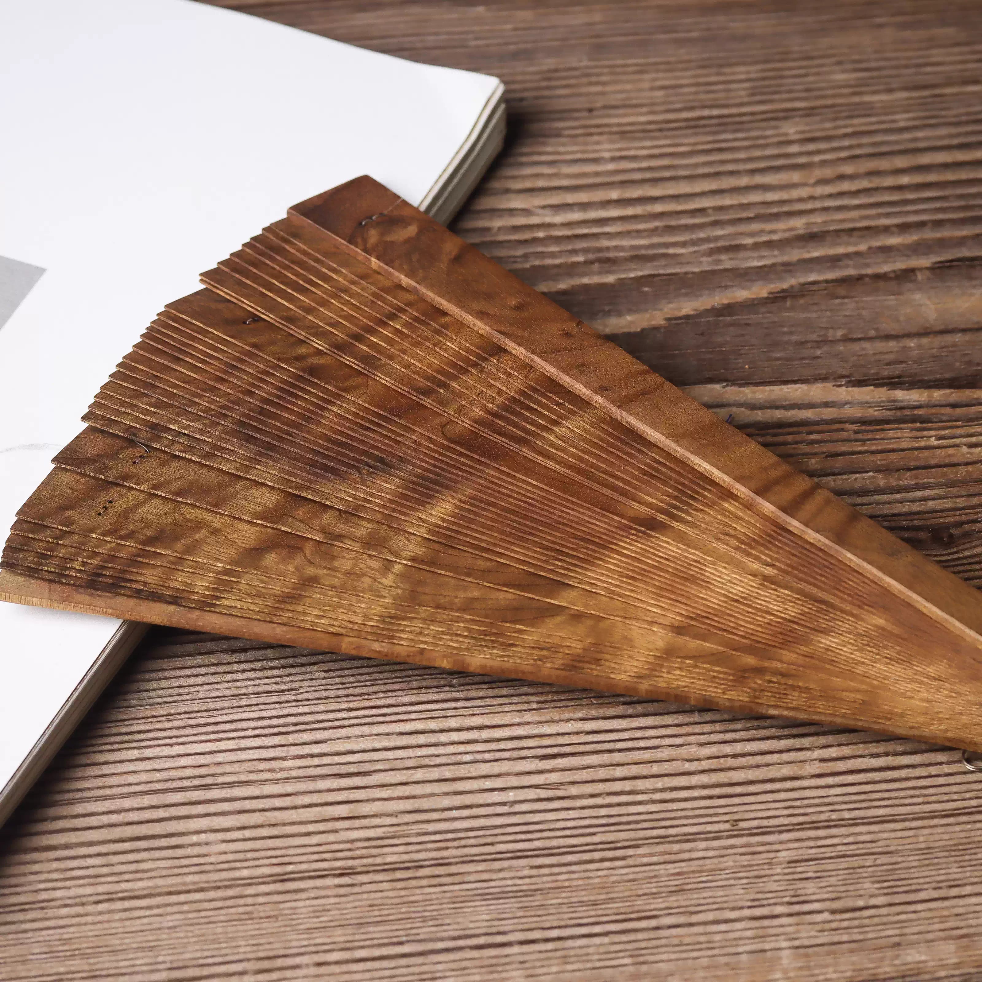 Close-up of golden nanmu wood folding fan with fine grain texture on wooden surface