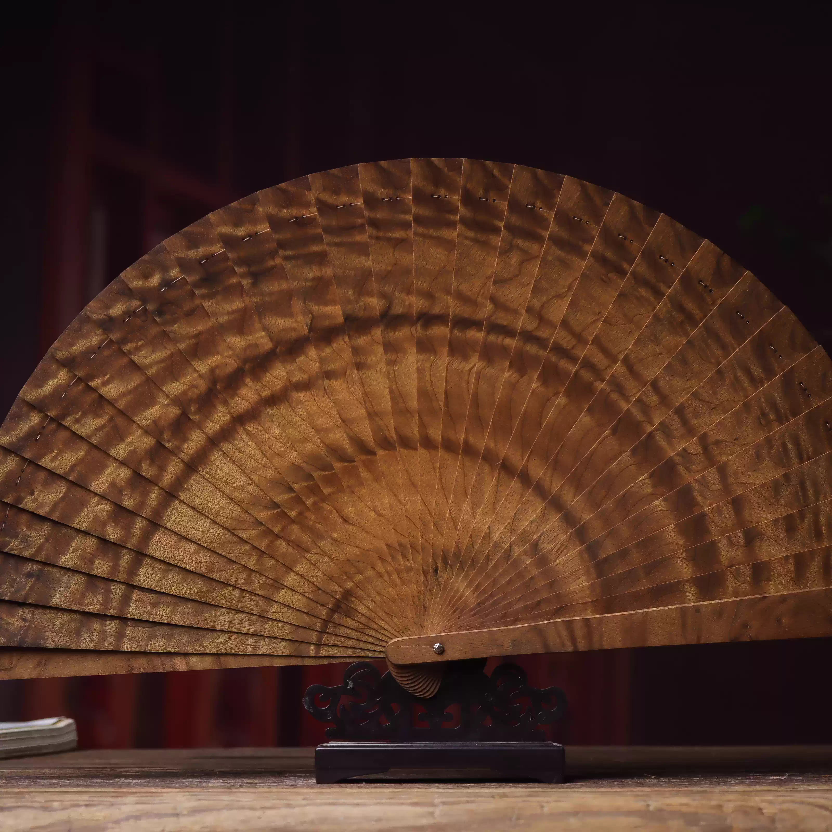 Golden nanmu wood folding fan displayed on wooden stand with intricate grain details
