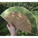 Rin Essense green and natural wood hand folding fan with delicate leaf design held in hand outdoors