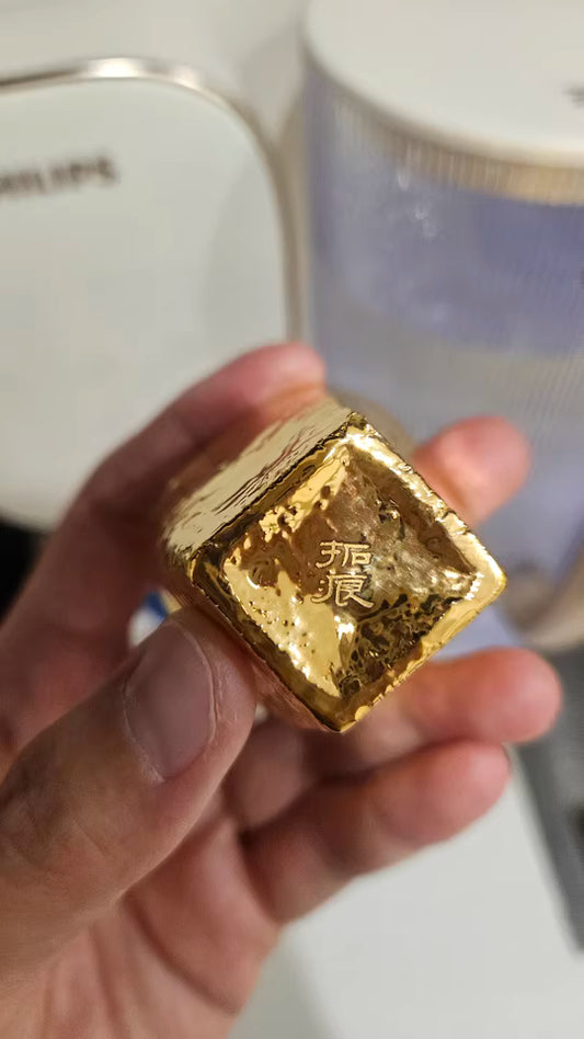 Hand holding a small gilded gold cup with Japanese characters engraved on it hand-shaped gilded Japanese cup