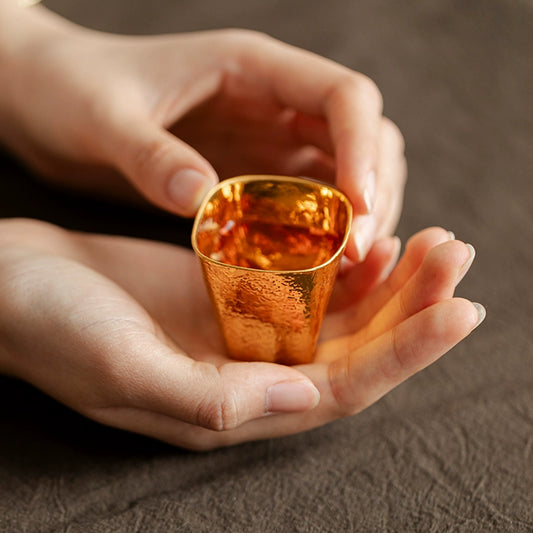 Hand holding a hand-shaped gilded Japanese cup with a textured gold surface by Rin Essense