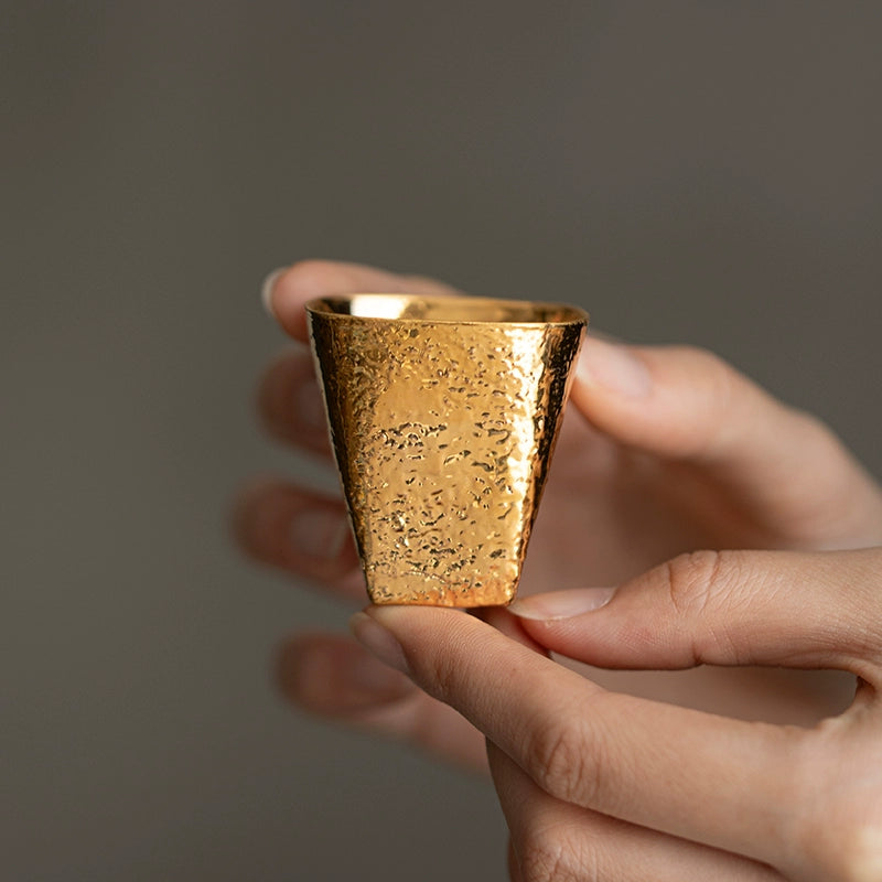 Hand holding a hand-shaped gilded Japanese cup with textured gold finish by Rin Essense