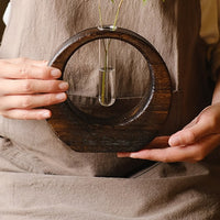 Rin Essense Japanese vase with circular wooden frame and single glass tube held by person in beige apron