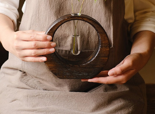 Rin Essense Japanese vase with circular wooden frame and single glass tube held by person in beige apron