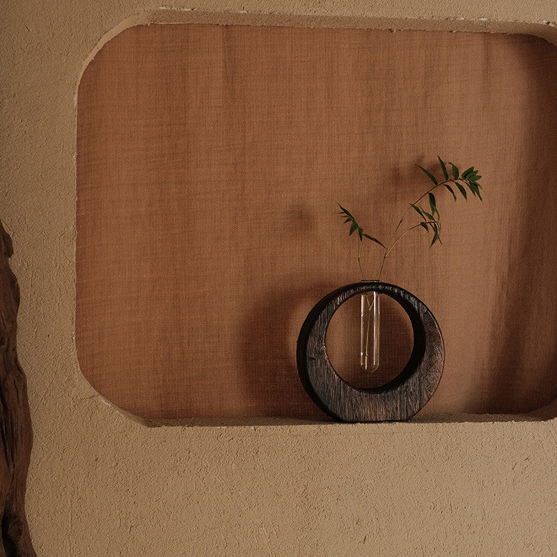 Rin Essense japanese vase with circular wooden frame and glass tube holding green leaves on beige textured background