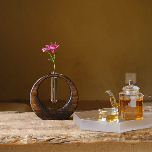 Rin Essense japanese vase with circular wooden frame and single pink flower on rustic wooden table