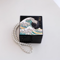 Rin Essense black lacquer jewelry box featuring a detailed wave design with a pearl necklace beside it