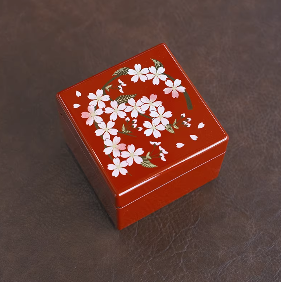 Rin Essense red jewelry box with white floral design on top placed on brown surface