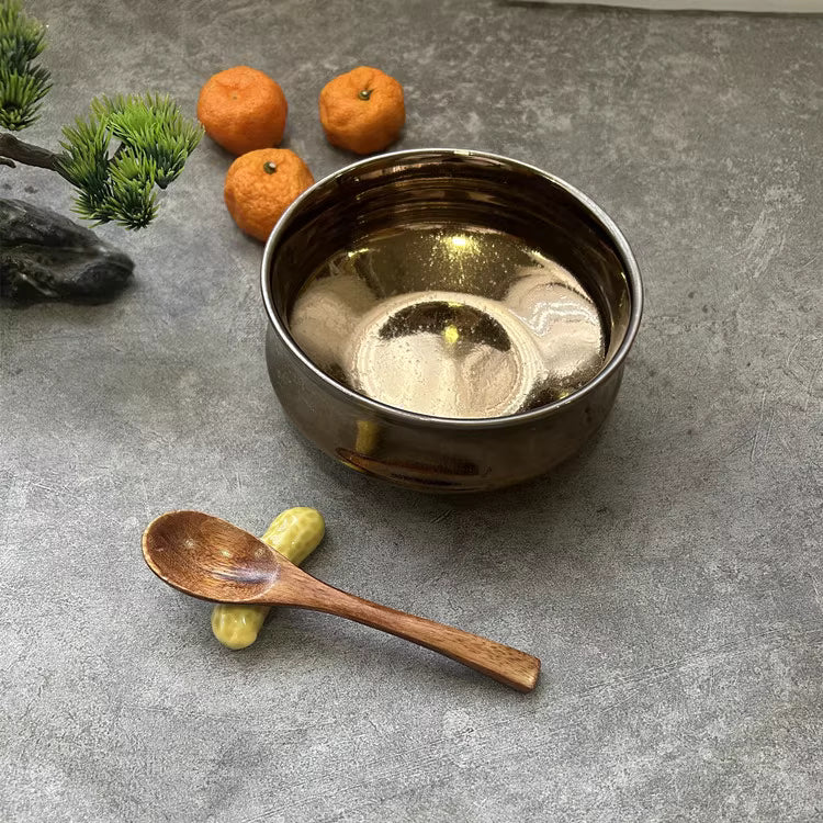 Shiny dark metal rice bowl with wooden spoon and three small oranges on gray surface by Rin Essense