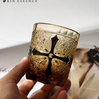 RIN ESSENCE whiskey glass with amber tint and black cross design held in hand
