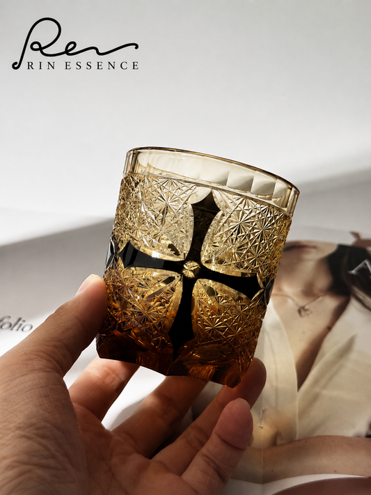 RIN ESSENCE whiskey glass with amber tint and black cross design held in hand
