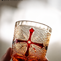 RIN ESSENCE whiskey glass with intricate red cross design held in hand with amber liquid