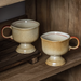 Two beige speckled Japanese vintage ceramic cup pedestal mugs with red rim and handle on wooden shelf