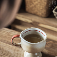 Japanese vintage ceramic cup with red rim and handle filled with tea on wooden table next to open book