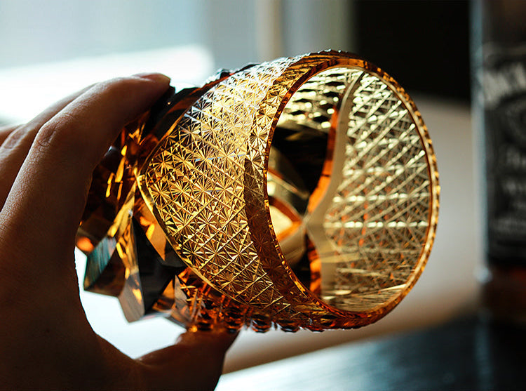 Handheld Rin Essense Satsuma Kiriko whiskey glass in amber cut crystal showing intricate geometric facets and shine