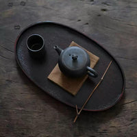 Rin Essense black oval tea tray with teapot and cup on rustic wooden surface