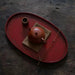 Rin Essense red oval tea tray with traditional brown teapot and bamboo tea utensils on wooden surface