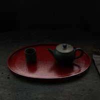 Rin Essense red oval tea tray with a black teapot and matching cup on a dark surface