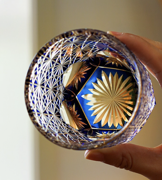 Edo Kiriko whisky glass with blue and gold starburst cut glass held by hand showing intricate geometric patterns