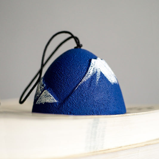 Rin Essense blue textured dome pendant with white mountain design and black cord resting on a book