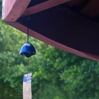 Rin Essense blue Japanese ceramic wind chime hanging from porch eave with paper strip and blurred trees
