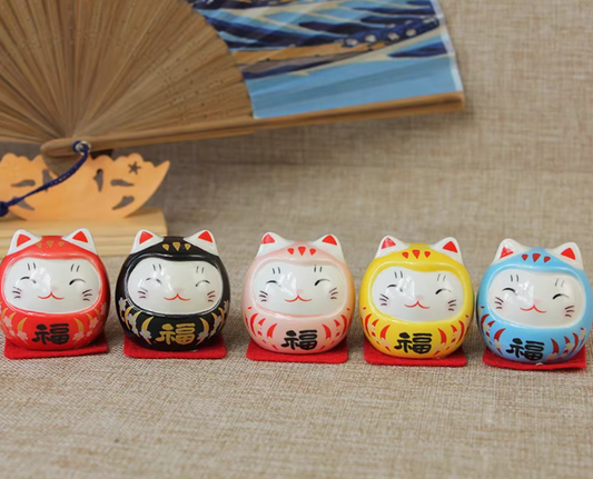 Five colorful ceramic cat daruma tumbling doll ornament figurines in red black white yellow and blue