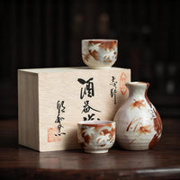 Rin Essense ceramic sake cup set with traditional brown and white design next to wooden box with Japanese calligraphy