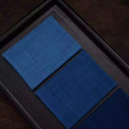 Japanese Indigo Tea Cloth – Hand-Dyed Cotton Linen in various shades of blue neatly folded on a dark tray