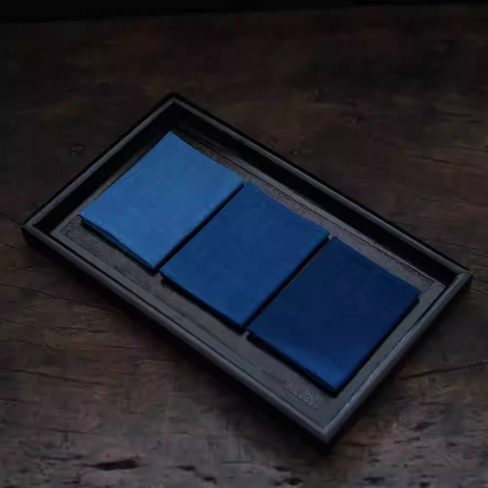 Japanese Indigo Tea Cloth – Hand-Dyed Cotton Linen in three shades of blue folded neatly on a dark wooden tray